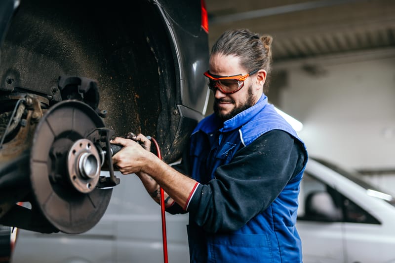 Ein Mechaniker mit Schutzbrille arbeitet an der Bremsscheibe eines Fahrzeugs auf der Hebebühne