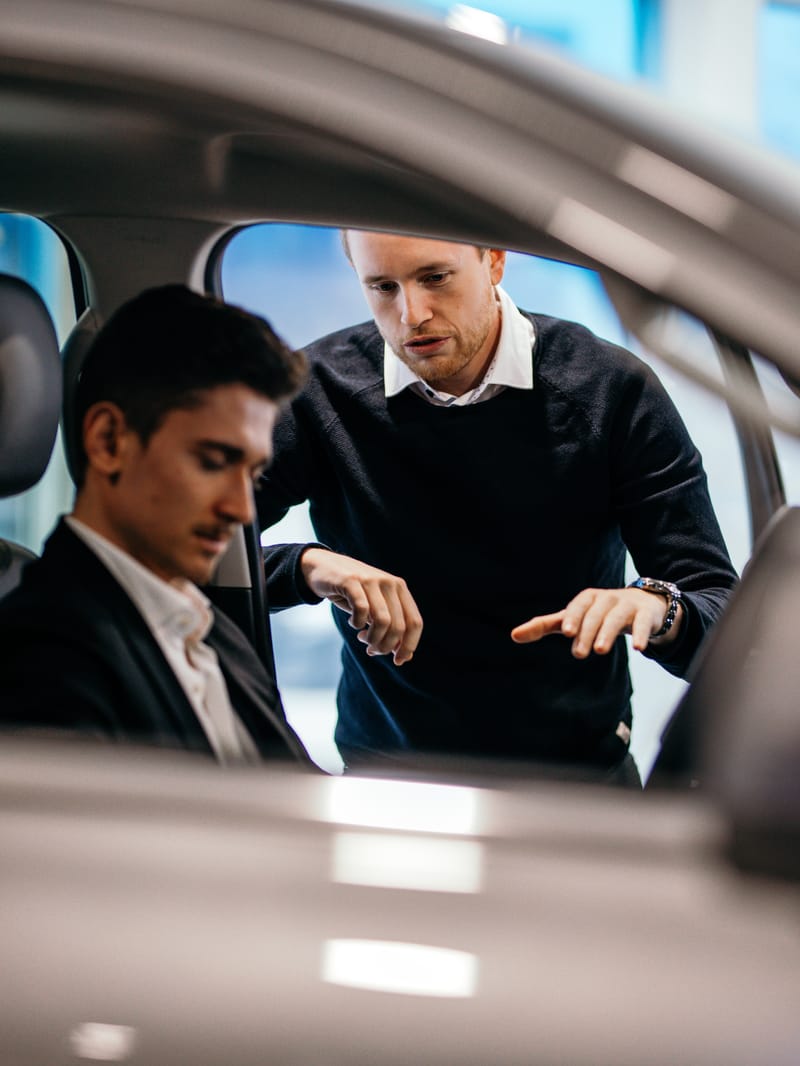 Ein Verkaufsberater zeigt einem Kunden im Fahrzeug die Bedienung