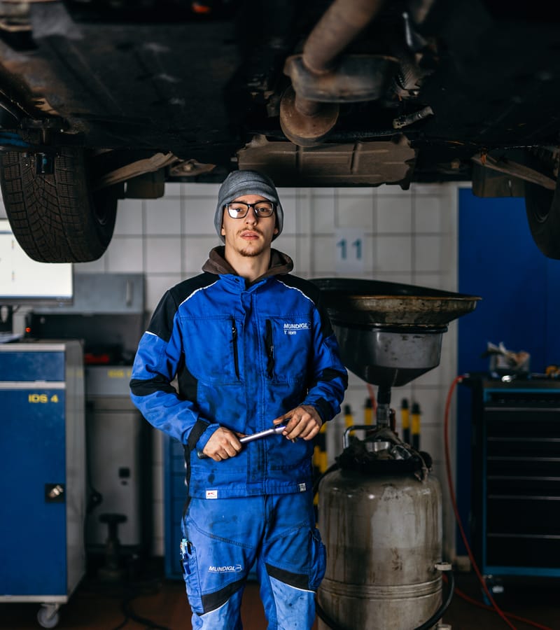 Ein junger Mechaniker steht mit Werkzeug unter einem Fahrzeug auf der Hebebühne