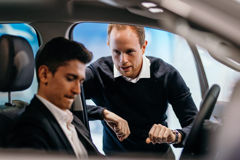 Ein Verkaufsberater erklärt einem Kunden im Fahrzeug die Ausstattung